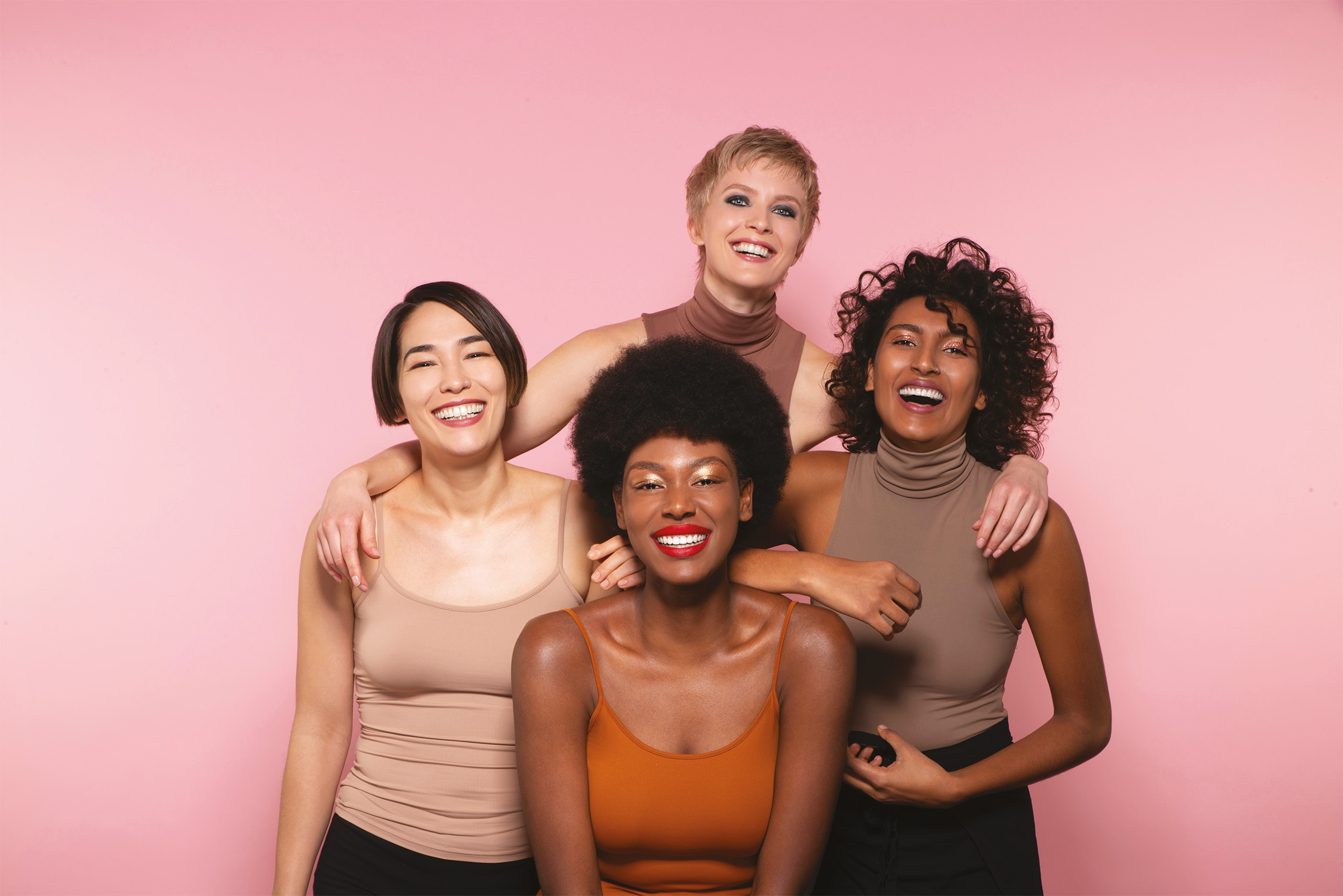 Four women smiling together on a pink background